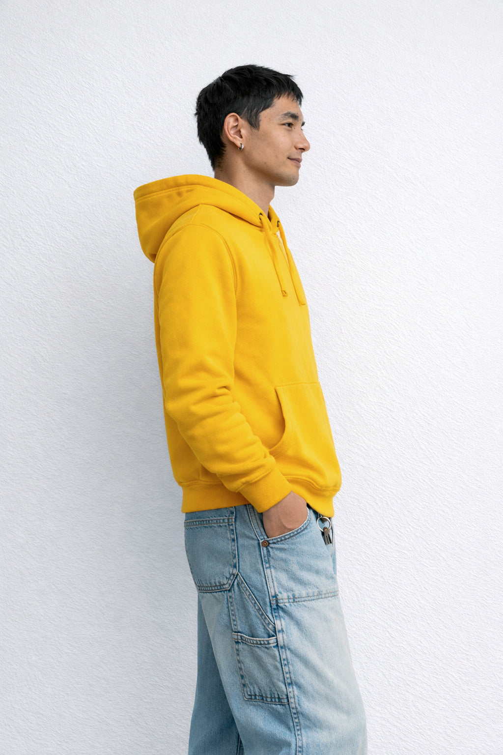 Person wearing a yellow hoodie and light blue jeans against a white background
