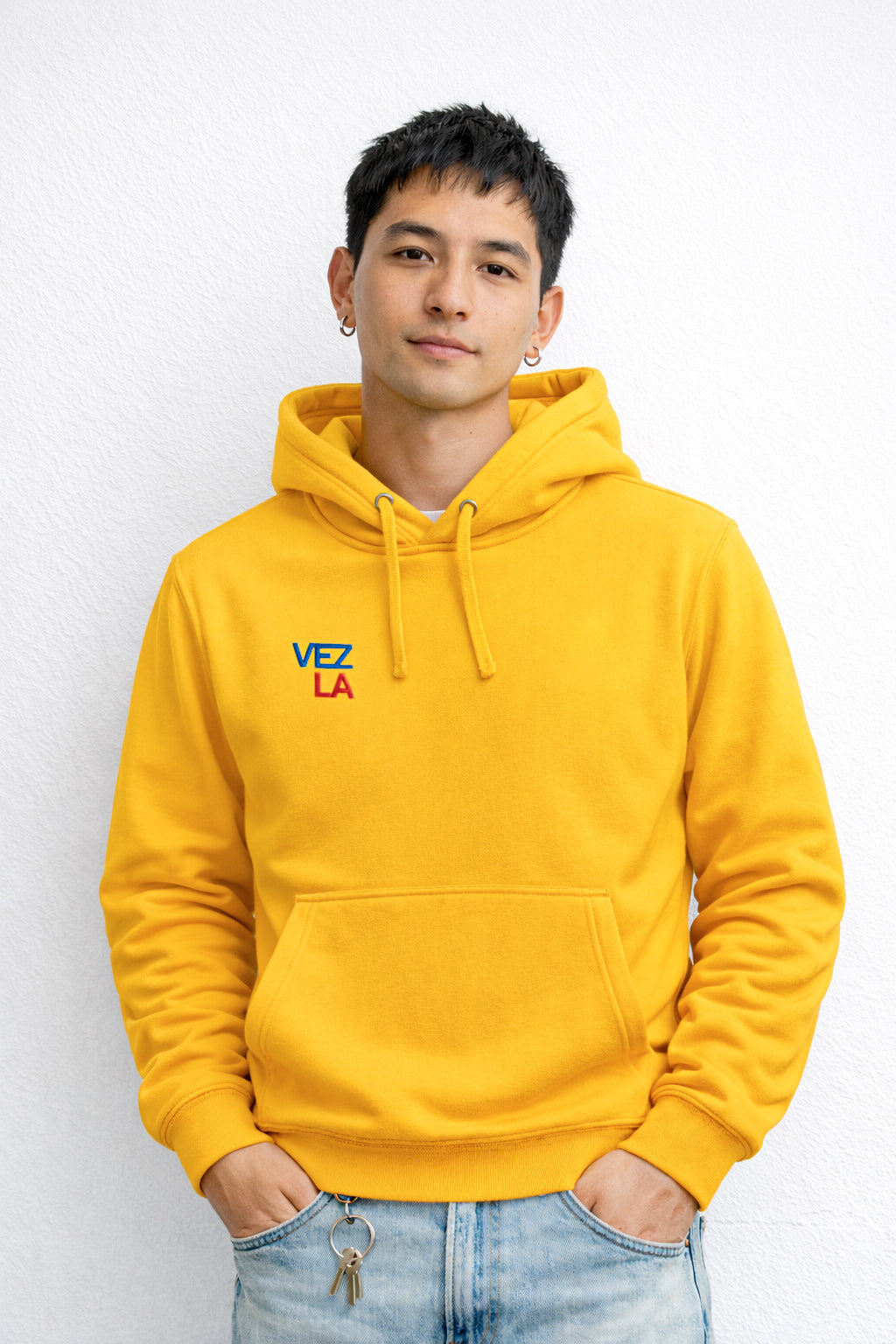 Person wearing a yellow hoodie with 'VEZ LA' logo against a white background